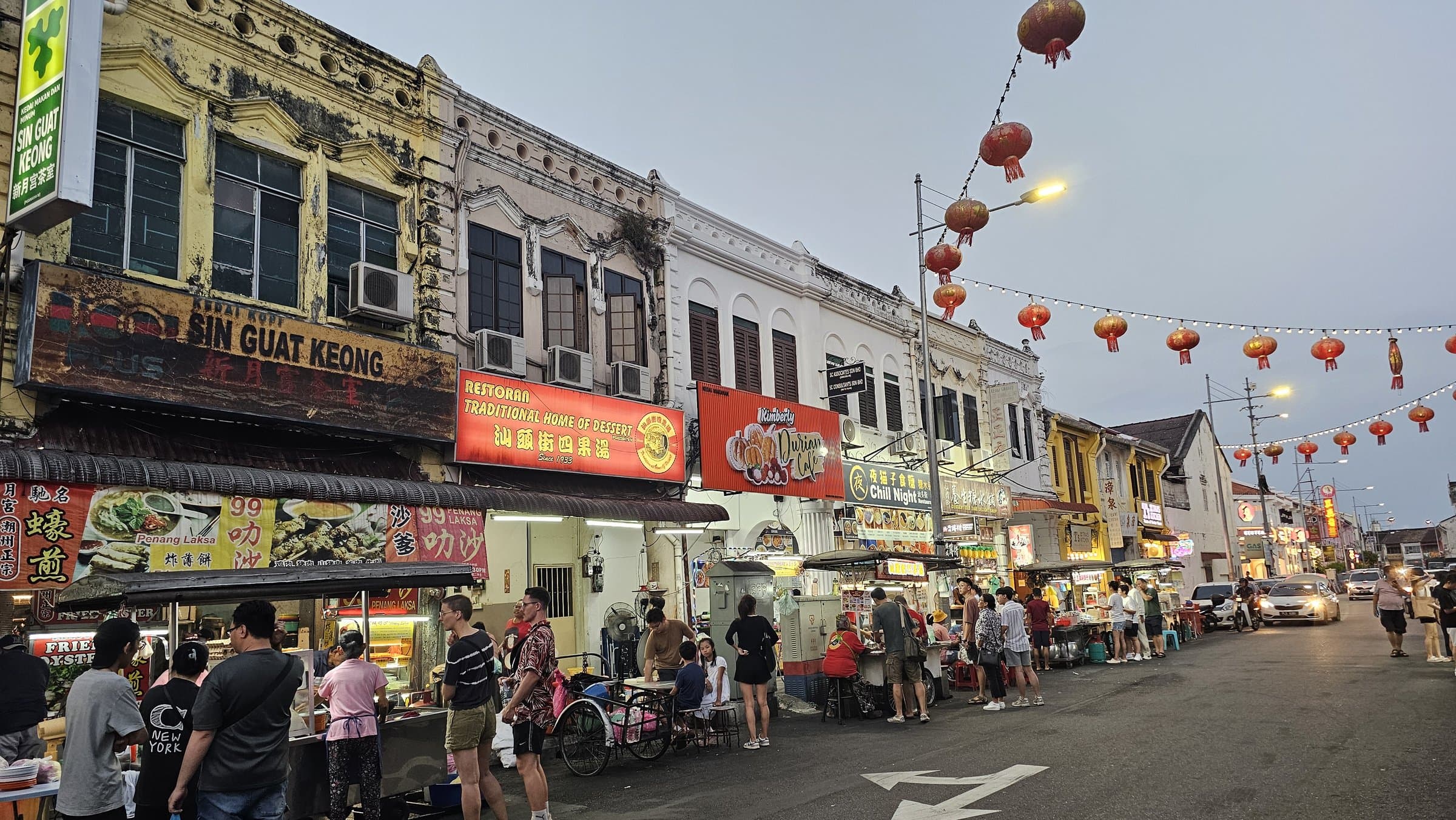 Red lanterns strung above a hawker street lined with old shophouses in George Town's Chinatown at dusk