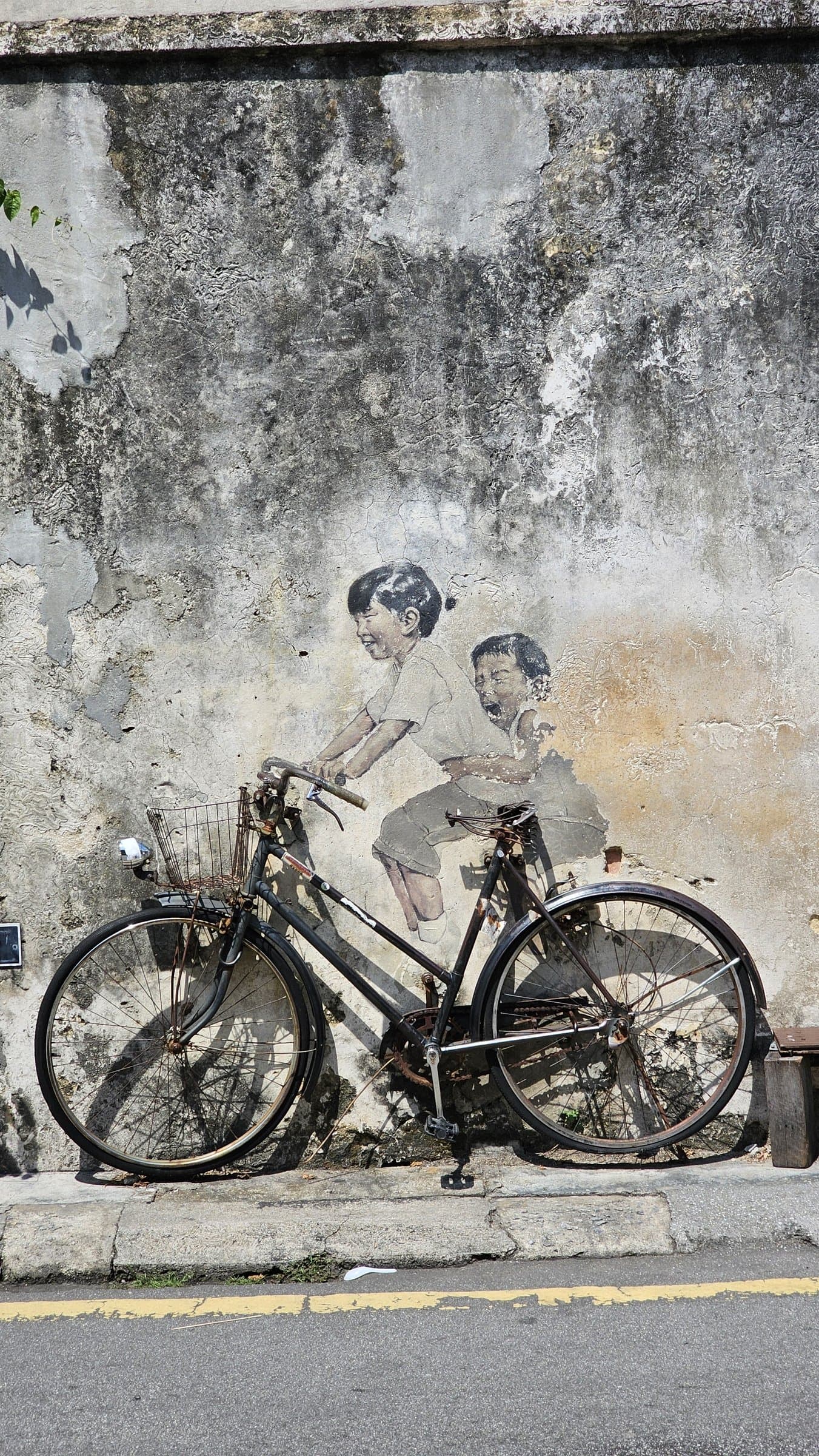 Ernest Zacharevic's 'Children on a Bicycle' mural, with a real bicycle leaning against a painted wall in George Town